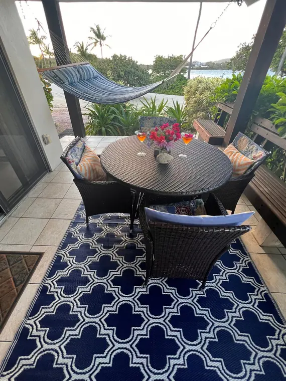 Covered patio of Sapphire Beach Condo D101 with hammock, table and the water behind &mdash; the video starts here
